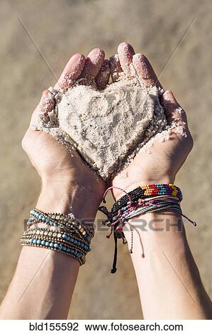 Stock Image - Close up of hands of Caucasian woman holding sand in heart shape. Fotosearch