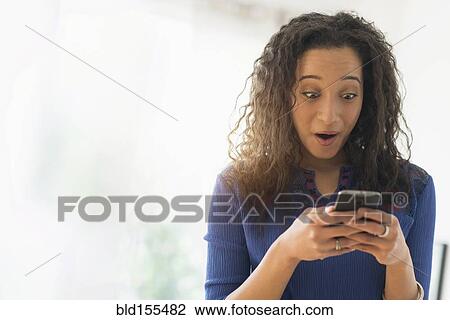 Stock Image - Close up of mixed race woman gasping at cell phone. Fotosearch