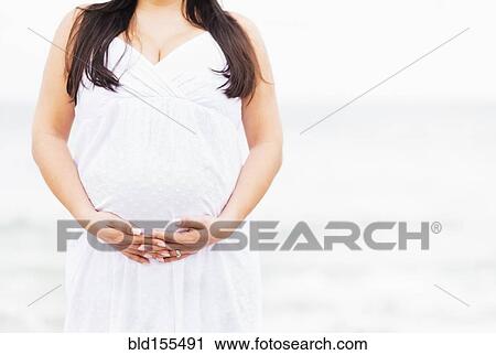 Stock Image - Close up of mixed race woman holding pregnant belly. Fotosearch