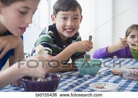 Stock Photograph - Close up of smiling children eating ice cream sundaes. Fotosearch