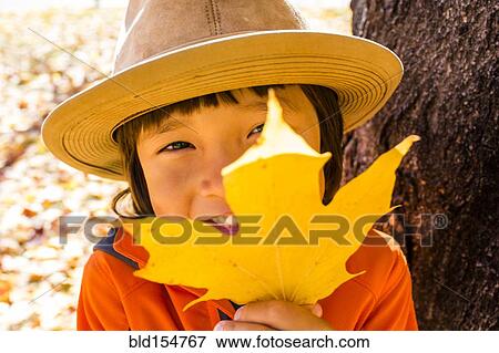 Stock Photo - Close up of smiling mixed race boy holding autumn leaf. Fotosearch