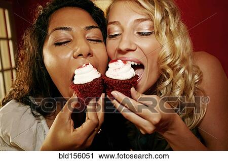 Stock Image - Close up of women eating red velvet cupcakes. Fotosearch
