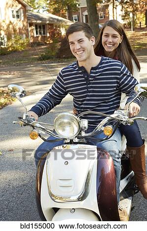 Stock Image - Couple riding scooter in suburban neighborhood. Fotosearch