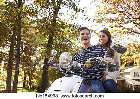 Stock Photo - Couple riding scooter in suburban neighborhood. Fotosearch