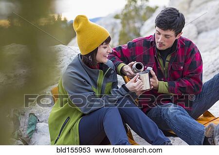Stock Image - Couple sharing coffee on rock formations. Fotosearch
