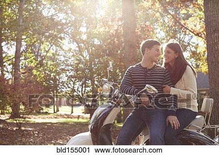 Couple sitting on scooter in park View Large Photo Image Stock Image - Couple sitting on scooter in park. Fotosearch