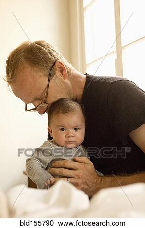 Stock Image - Father kissing baby boy on bed. Fotosearch