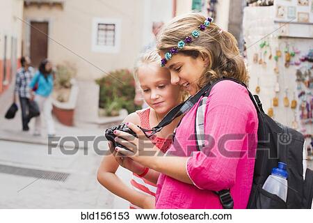 Stock Image - Girls looking at digital camera photographs on vacation. Fotosearch