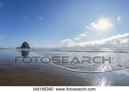 Stock Image - "Haystack Rock reflecting in ocean waves, Cannon Beach, Oregon, United States". Fotosearch