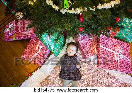 Stock Photography - High angle view of Caucasian baby girl laying under Christmas tree. Fotosearch