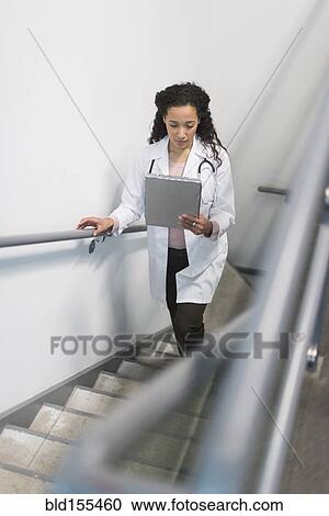 Stock Image - High angle view of mixed race doctor reading medical chart on staircase. Fotosearch