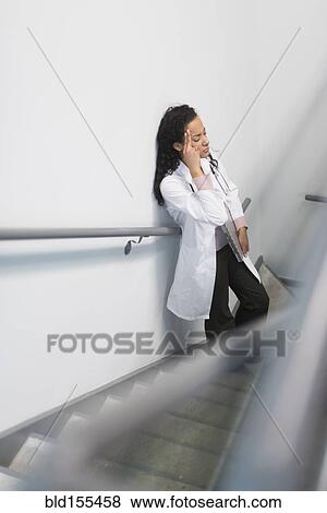 Stock Photo - High angle view of stressed mixed race doctor standing on staircase. Fotosearch