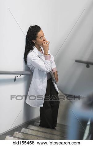 Stock Photograph - High angle view of stressed mixed race doctor standing on staircase. Fotosearch