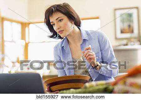 Stock Photo - Hispanic business owner eating salad in home office. Fotosearch