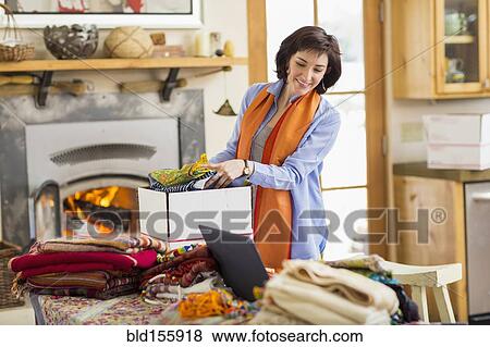 Stock Photo - Hispanic business owner packing boxes in home office. Fotosearch