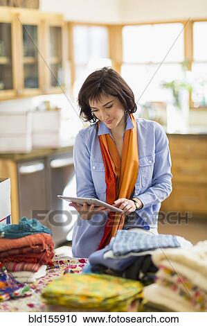 Stock Image - Hispanic business owner taking inventory with digital tablet in home office. Fotosearch