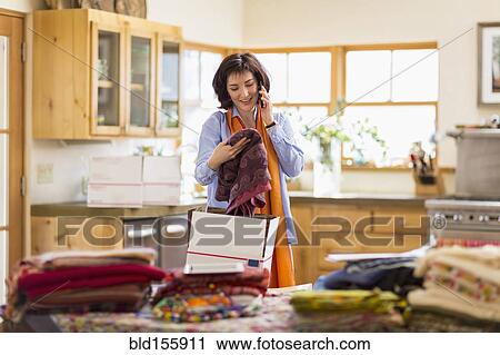 Stock Image - Hispanic business owner talking on telephone in home office. Fotosearch