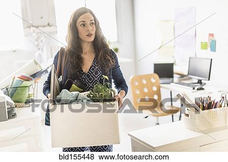 Stock Photo - Hispanic businesswoman carrying cardboard box in office. Fotosearch
