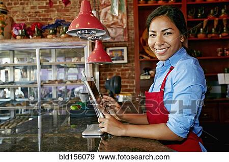 Stock Photo - Hispanic cashier using digital tablet register in bakery. Fotosearch