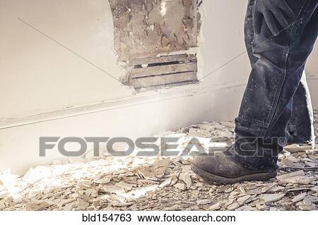 Stock Image - Hispanic construction worker standing in rubble of wall. Fotosearch
