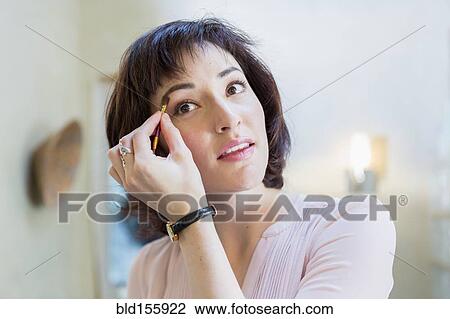 Stock Image - Hispanic woman applying makeup in mirror. Fotosearch