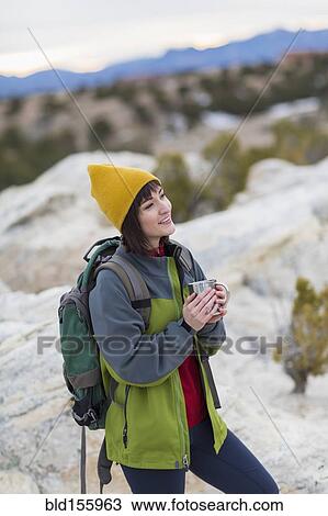Stock Image - Hispanic woman drinking coffee on rock formations. Fotosearch