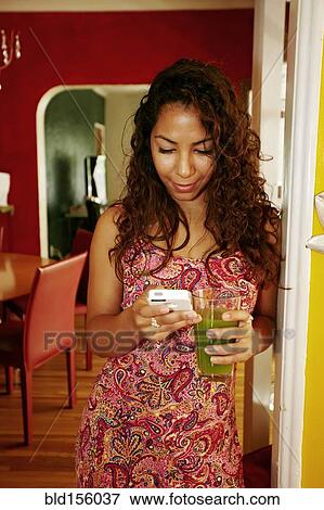 Stock Photo - Hispanic woman drinking green juice and using cell phone. Fotosearch
