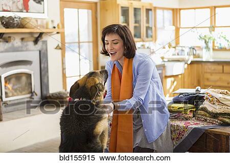Stock Photography - Hispanic woman petting dog in kitchen. Fotosearch