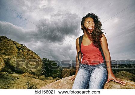 Stock Image - Hispanic woman sitting on rocky hilltop. Fotosearch