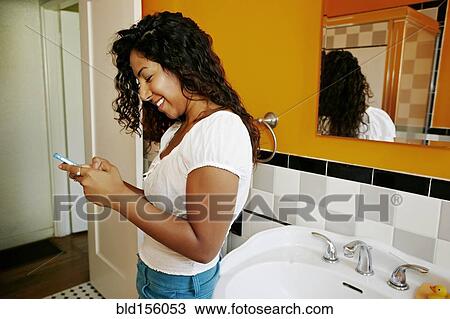 Stock Image - Hispanic woman using cell phone in bathroom. Fotosearch