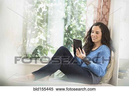 Hispanic woman using digital tablet in window sill View Large Photo Image Stock Photography - Hispanic woman using digital tablet in window sill. Fotosearch