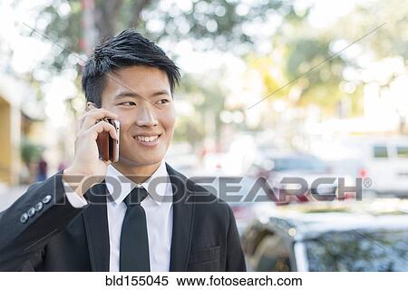 Stock Photography - Korean businessman talking on cell phone outdoors. Fotosearch
