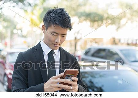Picture - Korean businessman using cell phone outdoors. Fotosearch