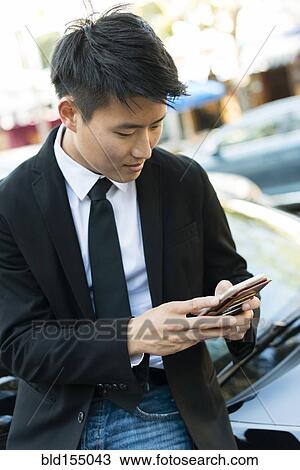 Korean businessman using cell phone near car View Large Photo Image Stock Image - Korean businessman using cell phone near car. Fotosearch