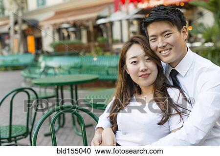 Stock Image - Korean couple hugging at sidewalk cafe. Fotosearch