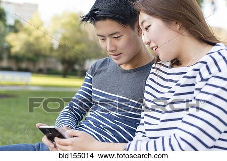 Picture - Korean couple using cell phone in park. Fotosearch