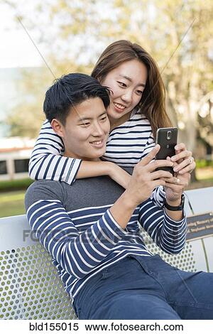 Stock Photography - Korean couple using cell phone in park. Fotosearch