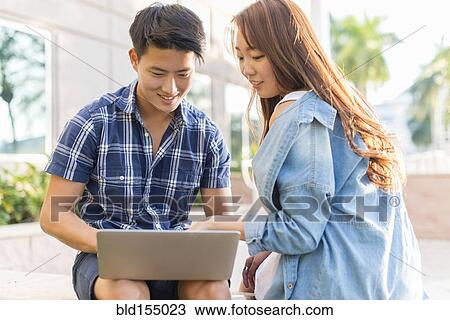 Stock Image - Korean couple using laptop outside building. Fotosearch