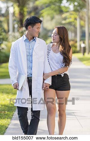 Stock Photo - Korean doctor walking with girlfriend on sidewalk. Fotosearch