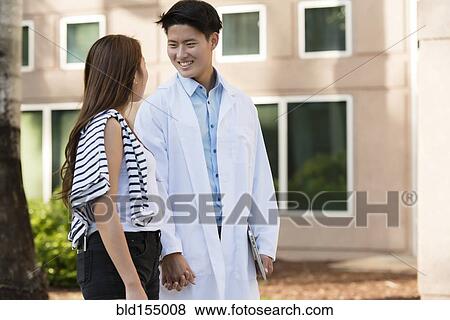 Stock Photo - Korean doctor walking with girlfriend outdoors. Fotosearch