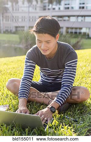 Stock Image - Korean man using laptop in grass. Fotosearch
