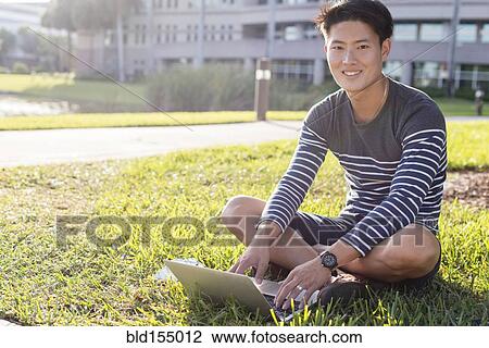 Korean man using laptop in grass View Large Photo Image Stock Image - Korean man using laptop in grass. Fotosearch
