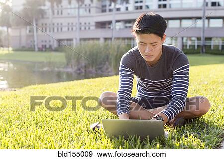 Stock Photo - Korean man using laptop in grass. Fotosearch