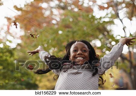 Stock Photo - Low angle view of African American girl playing in autumn leaves. Fotosearch