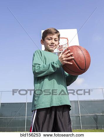 Stock Image - Low angle view of Caucasian boy holding basketball on court. Fotosearch