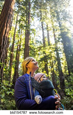 Stock Photo - Low angle view of Caucasian mother carrying daughter in forest. Fotosearch