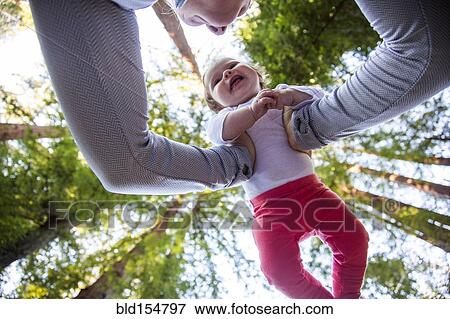 Stock Photo - Low angle view of Caucasian mother playing with baby under trees. Fotosearch
