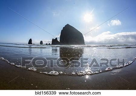 Stock Photo - "Low angle view of Haystack Rock reflecting in ocean waves, Cannon Beach, Oregon, United States". Fotosearch