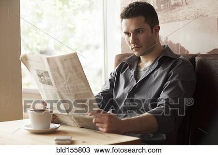 Stock Image - Man reading newspaper and drinking coffee in cafe. Fotosearch