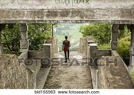 Stock Image - Man walking under stone walkway. Fotosearch